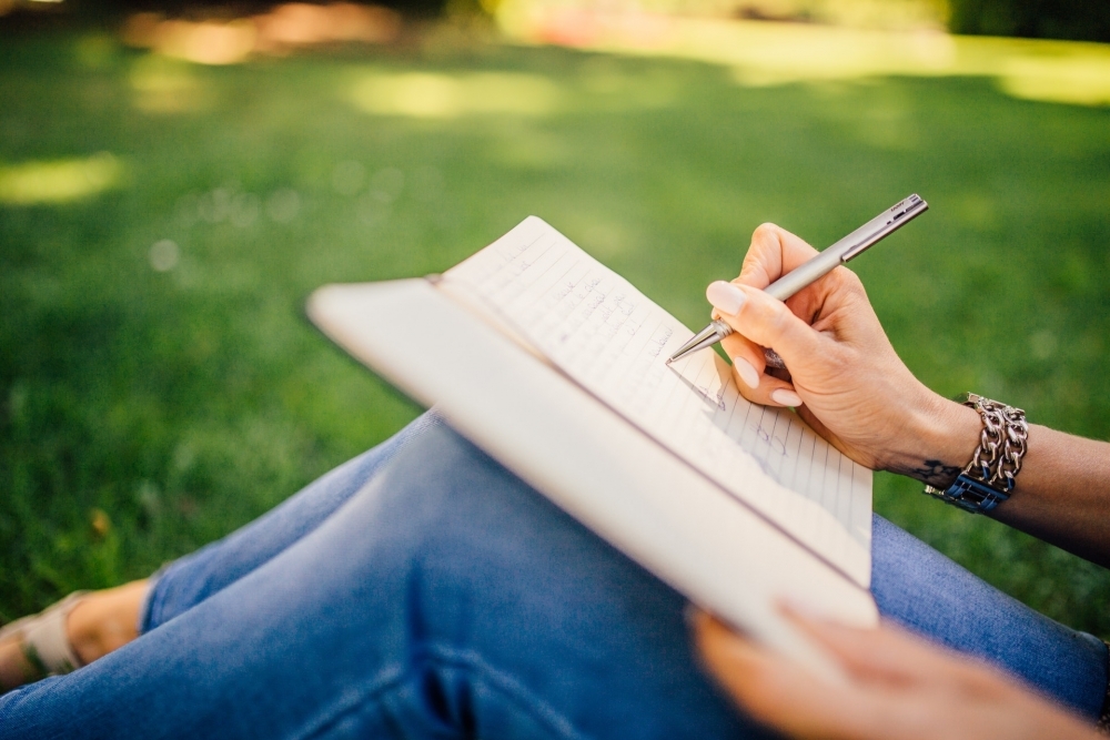 Woman sat on the grass writing in a notebook