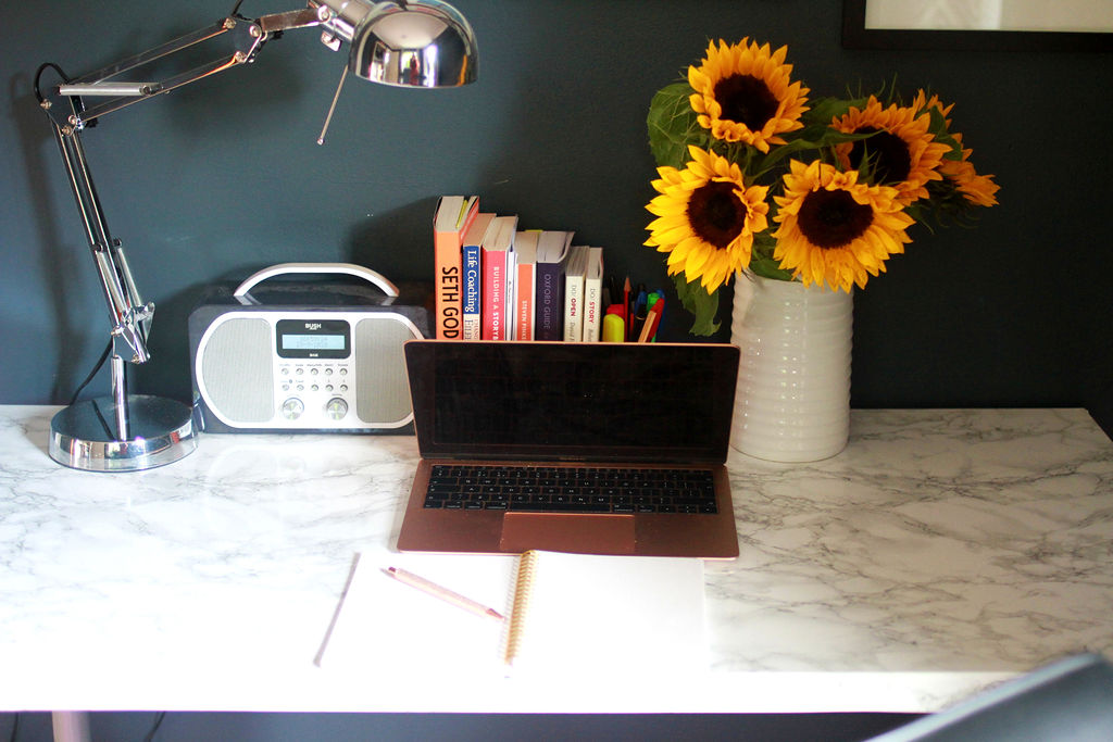 Harriet's desk, Mac, radio, angle poise lamp and white jug filled with sunflowers and stack of marketing and writing books
