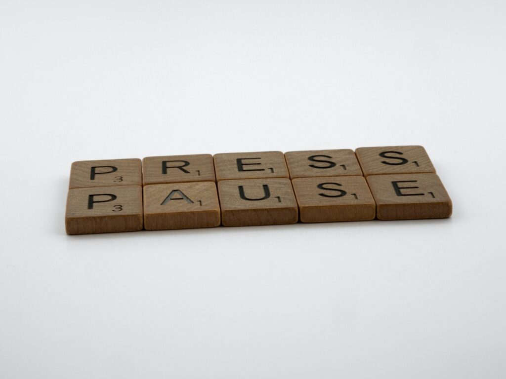 The words 'Press Pause' spelt out in small wooden scrabble letters on a white background