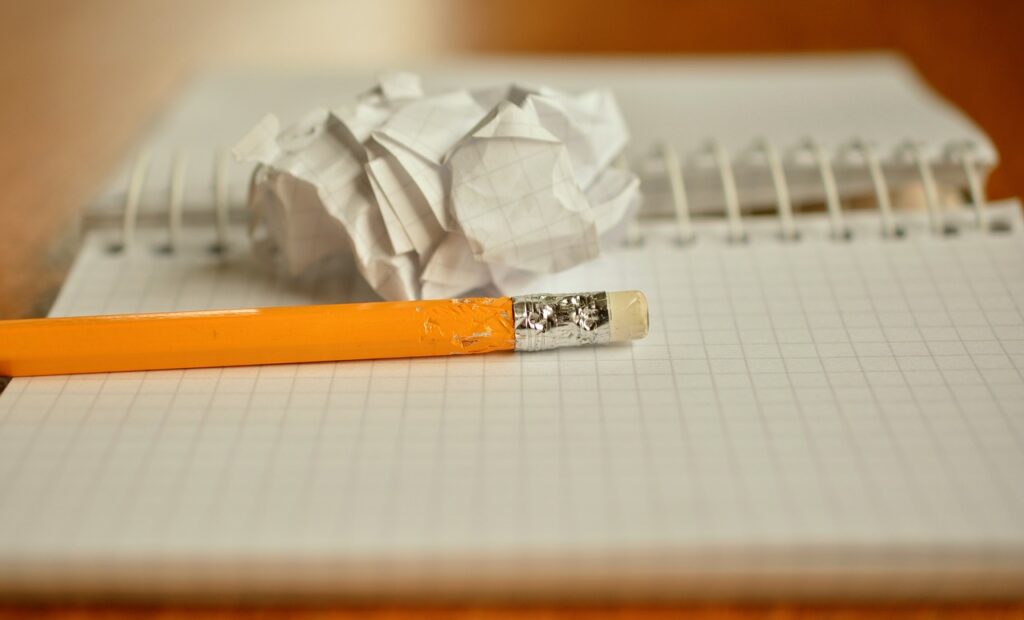 Close up of a ringbound notebook, empty pates, a crumpled piece of paper and yellow pencil resting on it