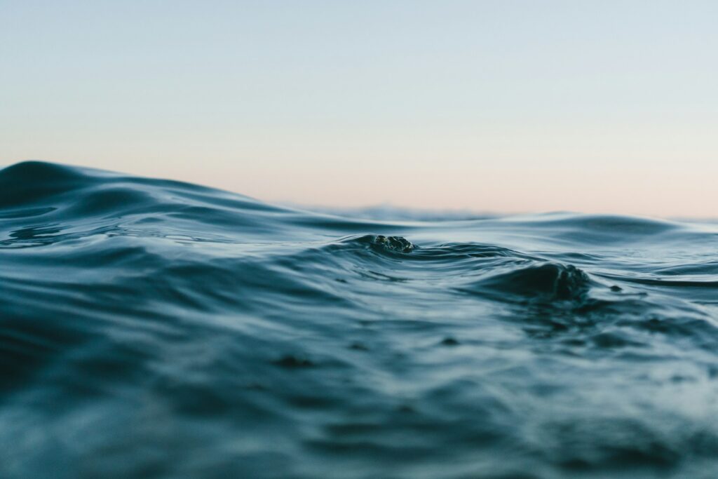 Close up of the sea, the water is a dark grey blue with small waves, ripples against a pale whoe. grey sky with a hint of apricot, maybe thhe end of a sunrise