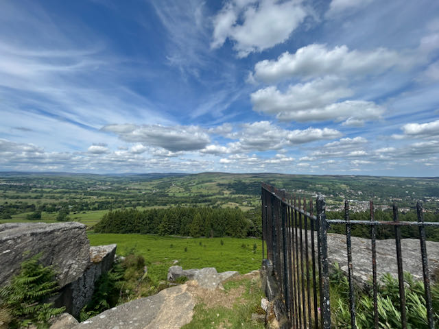 View from Swastika Stone on Ilkley Moor on a sunny day. Green landscape, blue sky and floating white clouds.