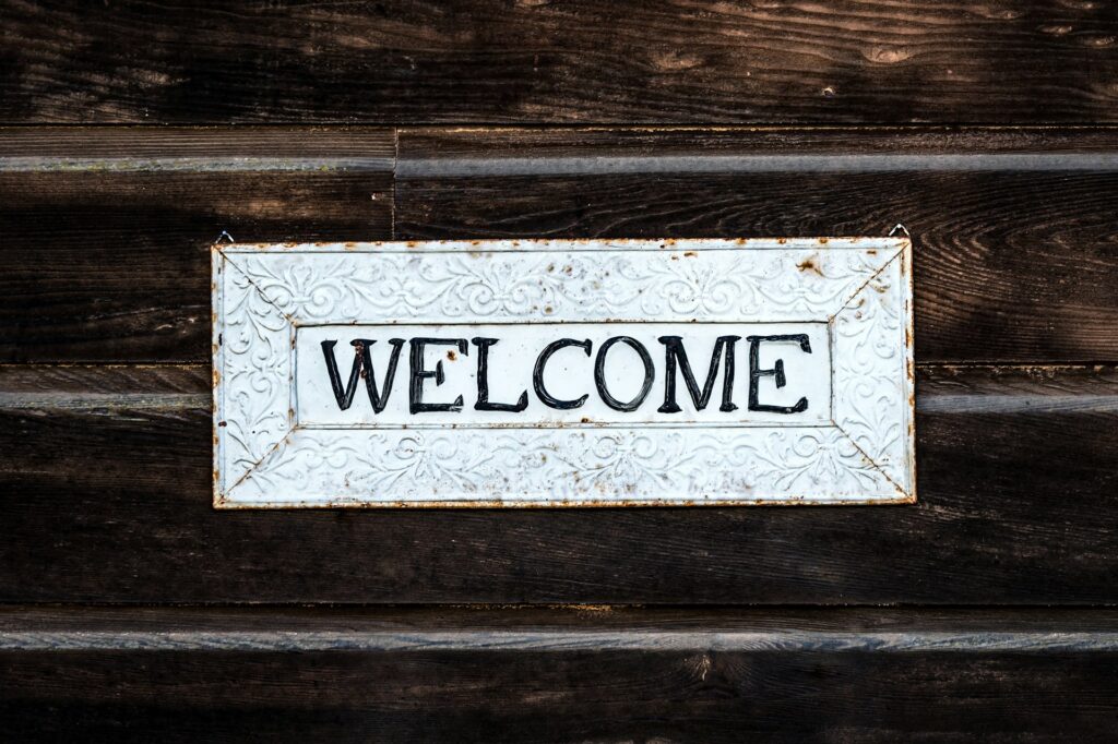 Whiteboard the shape of a horizontal letterbox with the word 'Welcome' spelled out in black traditional lettering on a wooden, shed like wall.